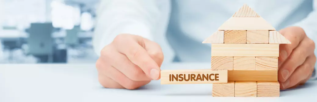 Hand placing a block labelled insurance into a house-shaped jenga structure